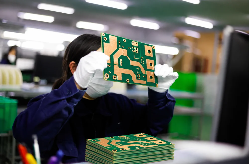 Factory worker inspecting a heavy copper bare PCB with matching boards stacked on the workbench
